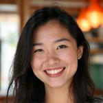 Sarah Kim, Community Manager at Veridian Bloom, a woman in her mid-30s with a warm and engaging smile. She is in a communal space, possibly a community center, with a backdrop of blurred happy faces, suggesting her role in fostering connections.